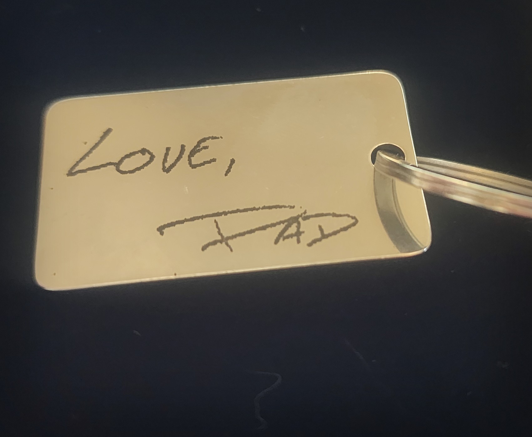 A stainless keyring engraved with a handwritten signature.